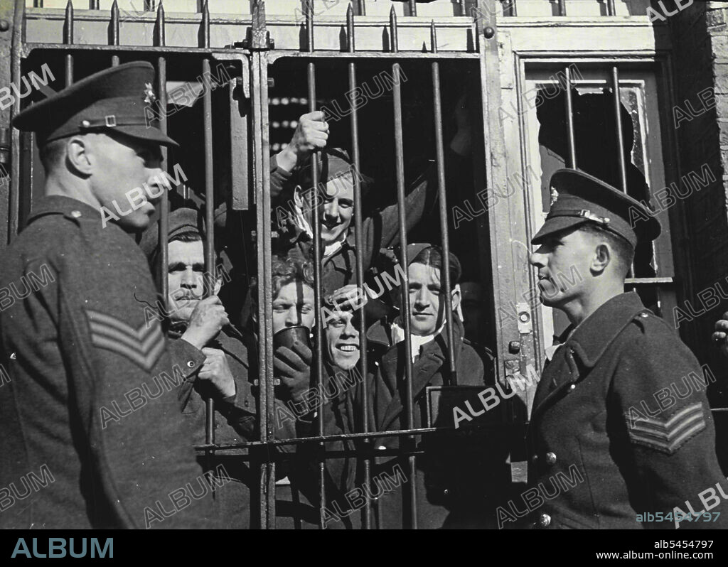 Wiggins... Staff -- Prison guards beside glasshouse gates, Prisoners inside. One hundred and fifty servicemen detained in the Aldershot Detention Barracks known as the "Glasshouse" and completely wreaked their barracks over the weekend. February 24, 1946.