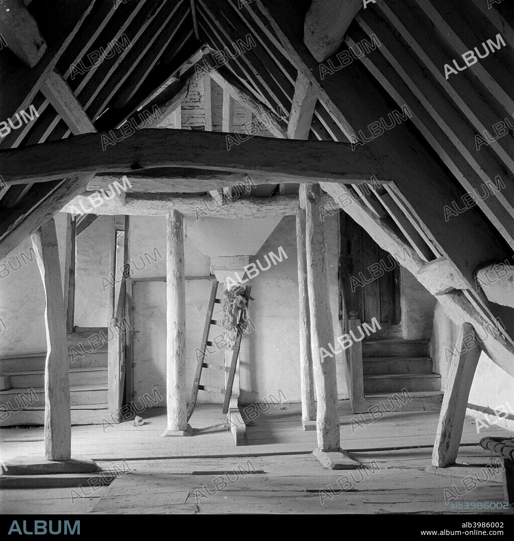 An attic in Kelmscott Manor, Oxfordshire, 1949. Wooden beamed attic with a ladder and staircases on either side of the chimney breast leading to bedrooms. The attics provided accommodation for servants. The manor, once the home of the artist William Morris, was built c1570 and enlarged the following century.
