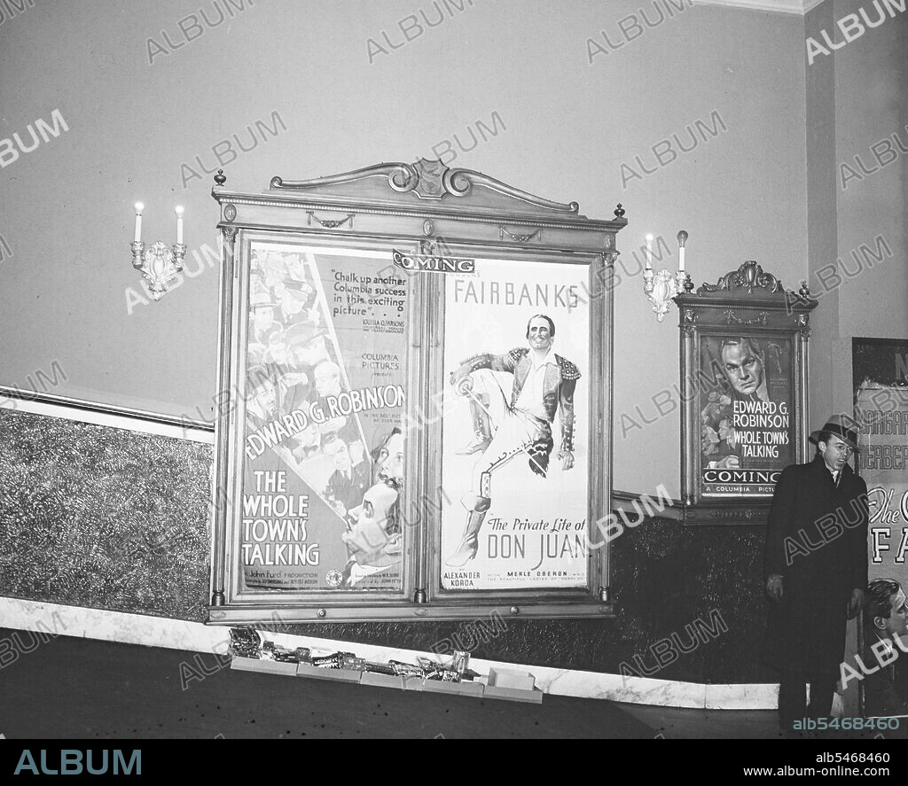 Man standing in movie theater lobby next to movie posters circa 1935.