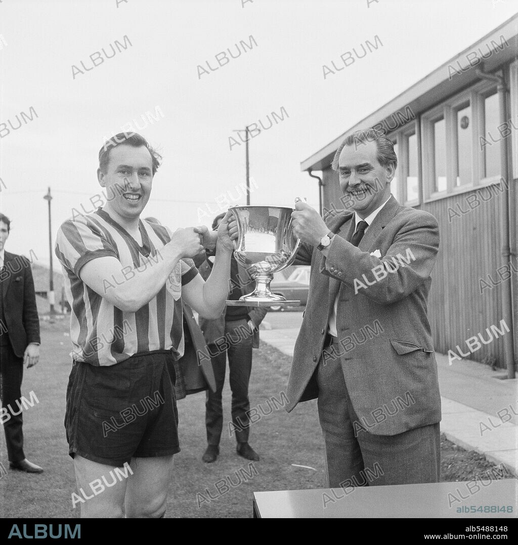 JOHN LAING PLC. Peter Hipkin, captain of the Laing Sports Club's 1st football team, 27/04/1963. Peter Hipkin, captain of the Laing Sports Club's 1st football team, being presented with the Senior Challenge Cup by V Ball, Vice-President of the London Commercial League. This image was published in June 1963 in Laing's monthly newsletter 'Team Spirit'. The Football Section of the Laing Sports Club had had a very successful season, with the 1st team winning every one of their games.