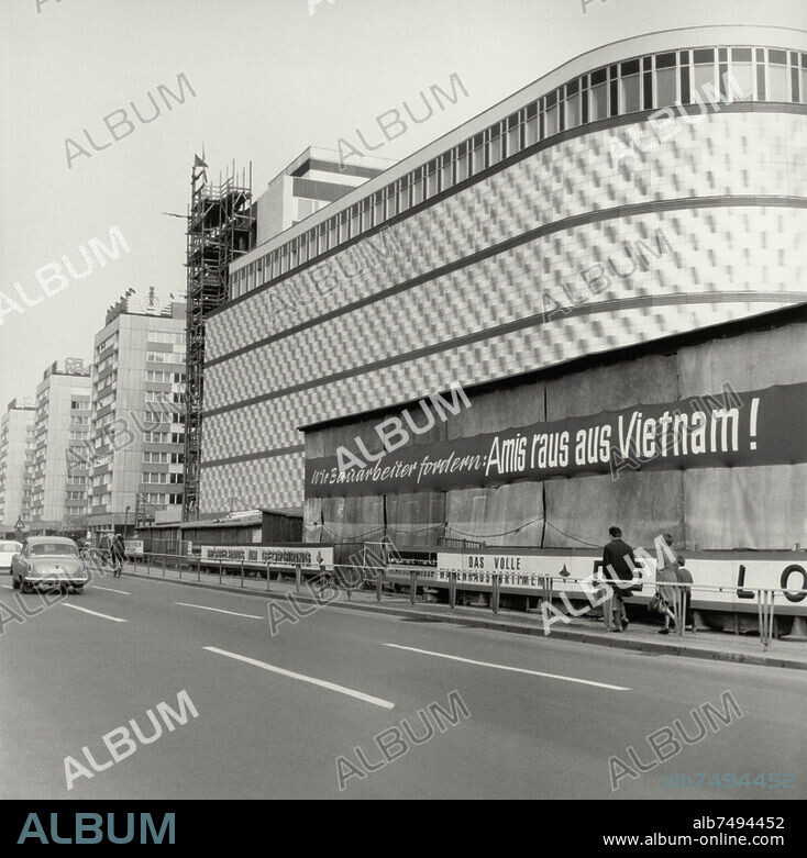 Leipzig (Sachsen; 1949-1990 DDR), Konsument-Warenhaus am Brühl, Richard-Wagner-Straße 20 (volkstümlich "Blechbüchse"; erbaut als Kaufhaus Brühl 1907/1908; Arch.: Emil Franz Hänsel; Metallfassade 1966 nach Konzeption von Harry Müller). Konsument-Warenhaus am Brühl (eröffnet 1968) mit Transparent "Wir Bauarbeiter fordern: Amis raus aus Vientnam!"; im Hintergrund drei Wohnblöcke (erbaut 1966). Foto, 1968.