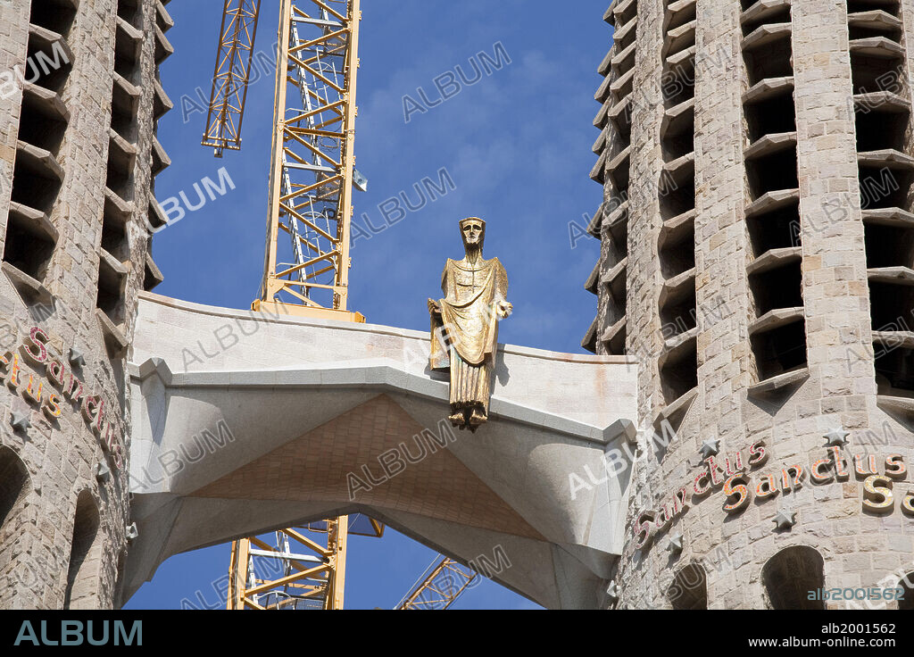 The construction of this unique Temple began in 1882, and one year later Antoni Gaudi was appointed Project Director. He worked on the project over 40 years until his death in 1926. The temple has three facades (named: 'Nativity', 'Passion' and 'Glory'), each bearing four souring towers. Seen here: on a bridge between the four bell towers of the Passion Facade (southwestern lateral facade), at a height of 198 feet, is a 26-foot-tall gold metallic representation of the resurrected Christ. The statue is the work of Josep Maria Subirachs. He began his work in 1987 following the ideas but not the style of Gaudi.