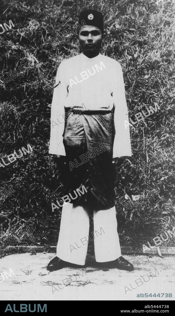 Malay R.A.F. Regiment Walking-out Dress has A Sarong!. A picturesque feature of this walking out dress, which has been approved for the Royal Air Force Regiment, Malaya, is the sarong of light blue interwoven cloth, with a vertical panel, worn to the rear, in the Royal Air Force colours of maroon, light blur and dark blue. The sarong, 36 inches deep, is worn form the waist to a little below the knees over white poplin long trousers made in the Malay style. The walking-out dress is completed by a white poplin shirt in Malay style and a blue-black Malay cap, known as a songkok, on the front of which is worn the Royal Air Force airman's badge. November 27, 1950.