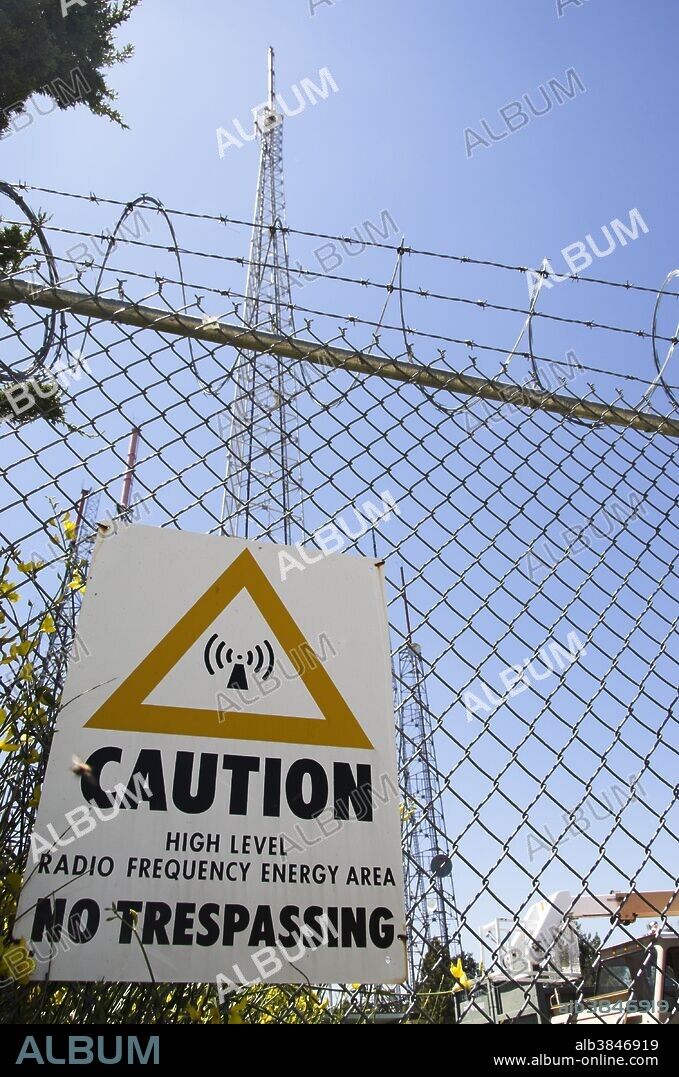 High-power RF radiation warning sign, Metromedia Center, Mt. Wilson, California, USA. High-power radio-frequency (RF) radiation such as that present near TV and radio broadcast towers can induce high currents in conductive objects, thus posing a strong shock or burn potential. US Federal agencies, Federal Communications Commission (FCC) and Occupational Safety and Health Administration (OSHA), recognize health hazards associated with high-power RF radiation. FCC limits the RF power density to which humans can be exposed. OSHA limits the value of induced current in working environments and issued a number of regulations pertaining to RF radiation hazards. Shown here is a high RF energy area warning sign posted on the fence surrounding the Metromedia Center on Mt. Wilson. The facility serves the Greater Los Angeles area and has a number of broadcast towers and satellite antennas.