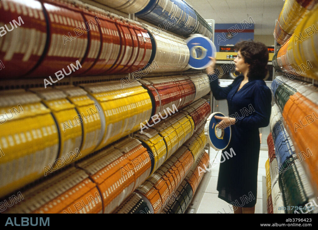Historic image of an old computer tape library, full of magnetic data storage tapes. Drives can be seen in the background.