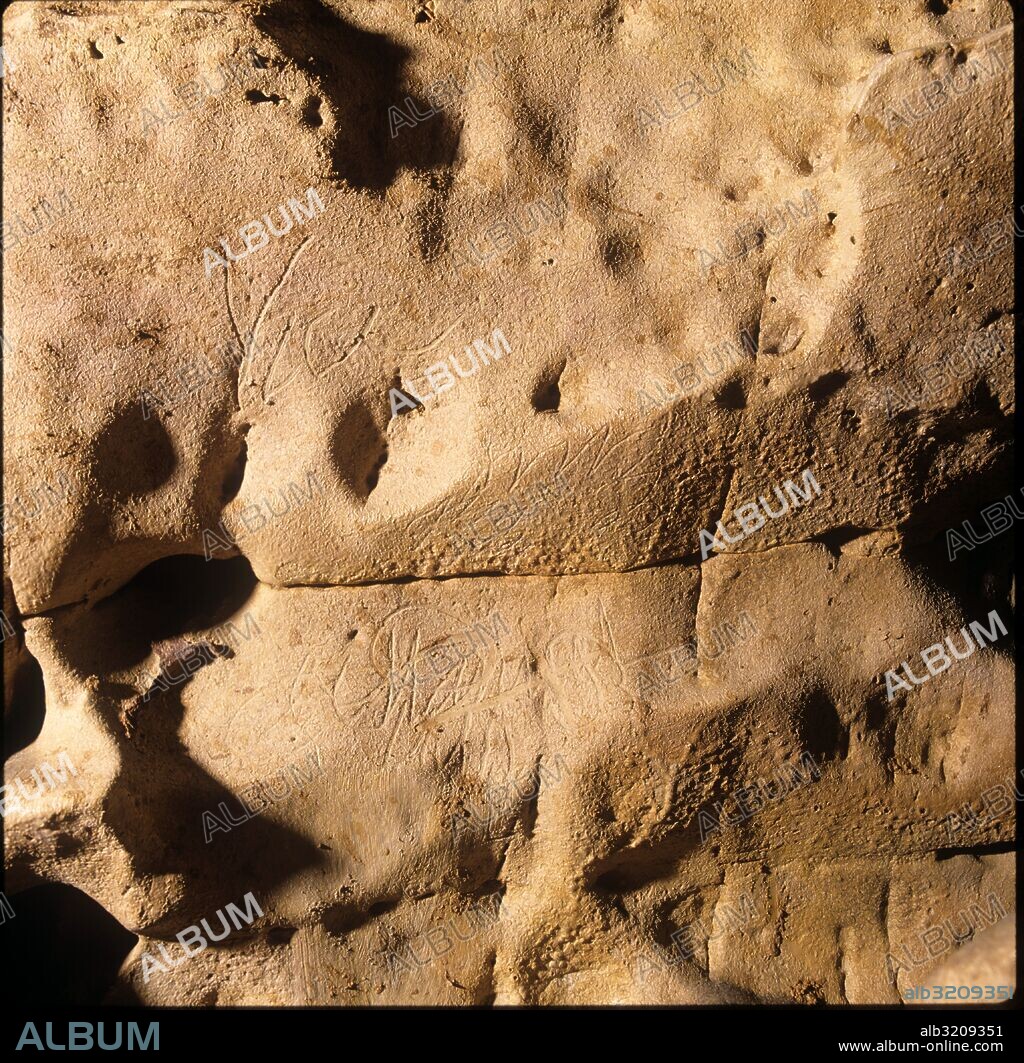CUEVA DEL REGUERILLO. FIRMA GRABADA. CERCA DE ELLA RECIENTEMENTE SE HA PINTADO UNA FLECHA EN BLANCO. PARED SUR AL ESTE DEL HUNDIMIENTO HASTA EL  CENTRO  DE LA SALA. MULTITUD DE FIRMAS. MAL CONSERVADAS CUBIERTAS DE BARRO.  MADRID, ESPAÑA.
