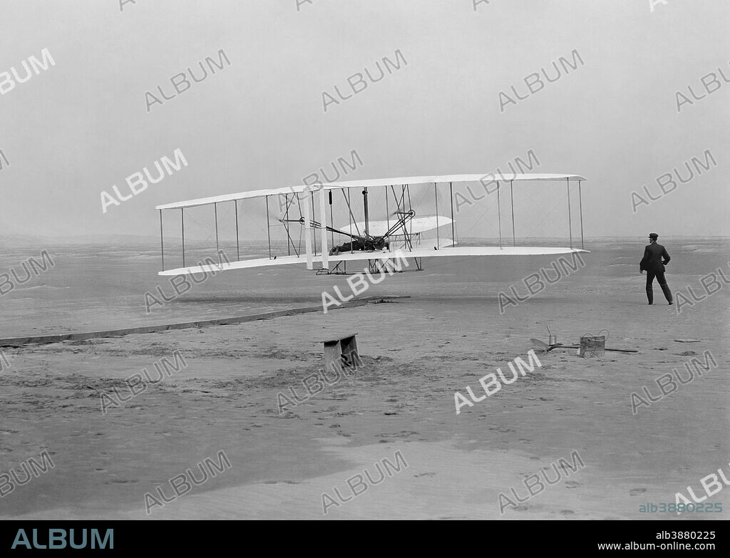 Vintage aviation photo featuring the first flight of the Wright Flyer on December 17, 1903 in Kitty Hawk, North Carolina. Orville Wright is piloting as brother Wilbur runs along beside.
