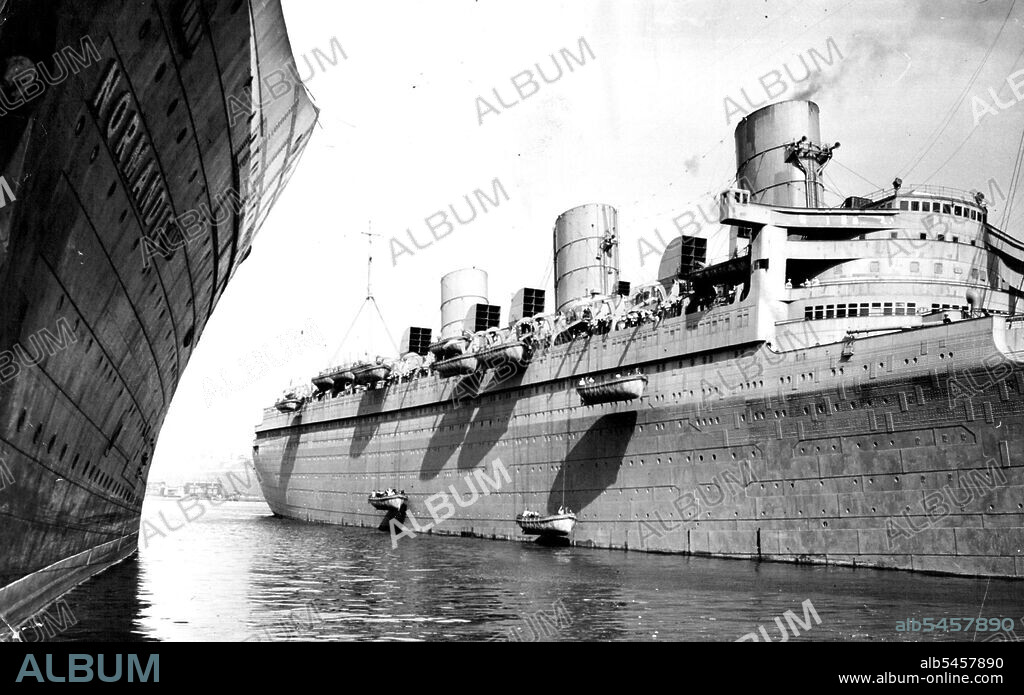 Queen Mary Preparing For Mystery Voyage -- Lifeboats being lowered into the water from the Queen Mary at her pier in New York today as preparations were made for quick departure. The Queen Mary received a large addition to her crew on Monday when 770 seamen arrived here on the S.S. Antonia and were divided between the Queen Mary and the Mauretania. In this photo the new crew members are operating the lifeboat mechanisms. No information has been given out by the Cunard white star line on the trip contemplated for the two giant liners. In the foreground is shown the S.S. Normandie sow of the French line. March 20, 1940. (Photo by Wide World Photo).