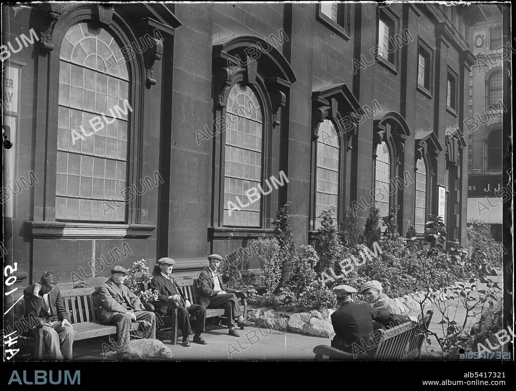 GEORGE BERNARD WOOD. Holy Trinity Church, Boar Lane, Leeds, 1941. An exterior view of the Holy Trinity Church, showing the south front with men sat on benches in the foreground. The church was built between 1721 and 1727 by William Etty. The upper tower was added after 1839 by R. D. Chantrell. It has a rectangular plan with seven by three bays, with a tower in the middle bay of the west end. The south front has a door in the first bay, windows with alternating triangular and segmental pediments on the ground floor, and a second tier above.