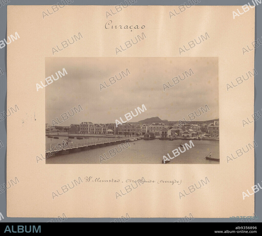 Willemstad, Otra Bande (Overzijde) (title on object), View of the Otrobanda (De Overkant), a district in Willemstad on Curaçao. In the foreground the Queen Emma Bridge. Part of a group of 44 photographs of Paramaribo, Suriname and Curaçao, c. 1900-1905, mounted on cardboard and inscribed., anonymous, Willemstad, 1900 - 1905, photographic support, cardboard, height 116 mm × width 189 mm.