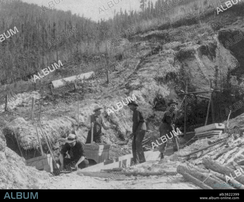 Placer mining for gold at Discovery Claim in the Klondike. The Klondike Gold Rush was a migration by an estimated 100,000 prospectors to the Klondike region of the Yukon between 1896-99. Gold was discovered by local miners on August 16, 1896 and, when news reached Seattle and San Francisco, it triggered a stampede of would-be prospectors. To reach the gold fields most took the route through the ports of Dyea and Skagway in Alaska. Here, the Klondikers could follow either the Chilkoot or the White Pass trails to the Yukon River and sail down to the Klondike. Each of them was required to bring a year's supply of food by the Canadian authorities in order to prevent starvation. In all, their equipment weighed close to a ton, which for most had to be carried in stages by themselves. Together with mountainous terrain and cold climate this meant that those who persisted did not arrive until summer 1898. Mining was challenging as the ore was distributed in an uneven manner and digging was made slow by permafrost. In the summer of 1899, gold was discovered around Nome in west Alaska, and many prospectors left the Klondike for the new goldfields, marking the end of the rush. Gold mining activity lasted until 1903. Photographed by William H. Rau, 1900.