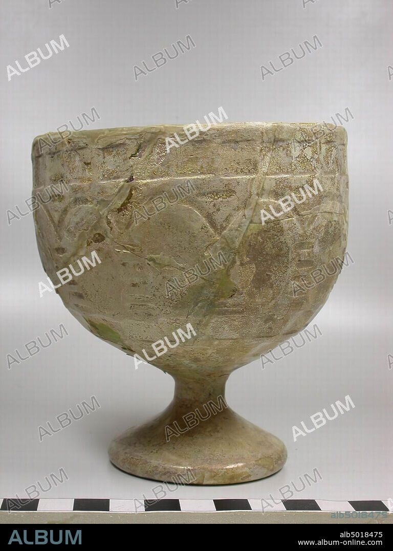 Glass cup on foot, almost identical pattern with no. 1 with the difference that the arcade pattern is bounded from above by just a row of square cut squares and not rounded from below, but two rows of square ground squares. The glass, originally pale sea green, has been given a dirt-white, lime-like color due to weathering. It has been broken into many pieces, but restored and complete. Late Sasanian., Crockery, glass, H 11.3 cm, D 10.5 cm, Sasanid Period 500-700 AD, Iran.