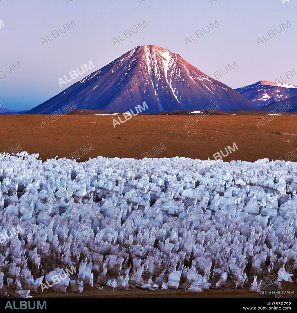 The spectacular Licancabur Volcano at the border between Chile and Bolivia. Licancabur appears in the morning twilight over an Andean ice field at an altitude of 5000 meters. The ice field in the foreground is a feature of high-altitude Andean plateaus known as ice penitentes. Licancabur reaches to 5920 meters. November 2011.