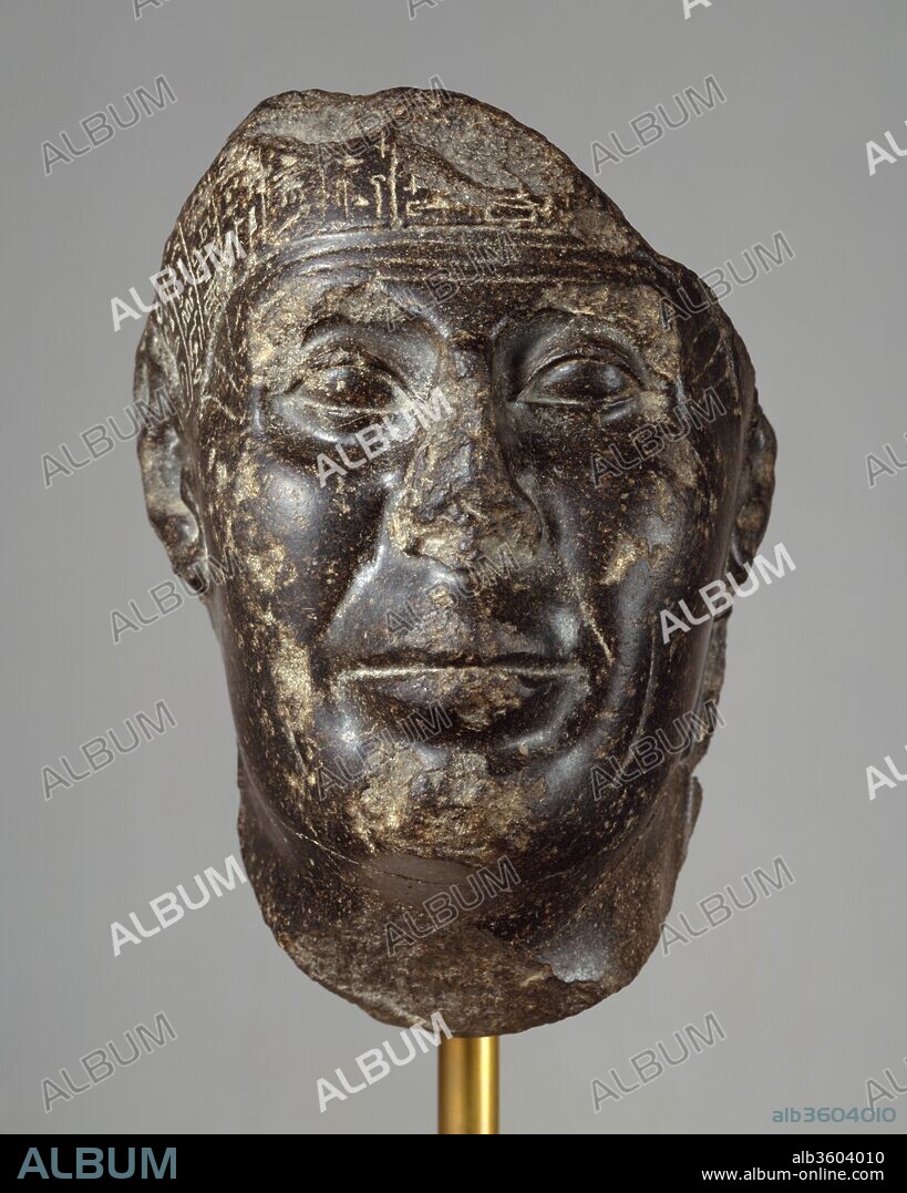 Head from a Statue with Magical Texts. Dimensions: H. 21.2 cm (8 3/8 in.); W. 14.5 cm (5 11/16 in.); D. 11.5 cm (4 1/2 in.). Dynasty: Dynasty 30. Reign: probably reign of Nectanebo II. Date: probably 360-343 B.C..
Magical texts like those on the Metternich stela (50.85) probably covered all but the face, feet, and hands of the statue to which this fragment belonged.  The statue would have stood in a temple where it could be visited by persons wishing to be healed.  Inscribed statues of this type can almost all be dated to the fourth century.
A man well-advanced in years is depicted, his skin soft and marked by fine creases but his small eyes and his wide mouth still sure.  Realistic representations are known from late Dynasty 26 and probably continued to be made during the Persian Period, although little can be assigned to that interval with certainty; thereafter they knew continuous popularity from the fourth century until the end of the Ptolemaic Period.