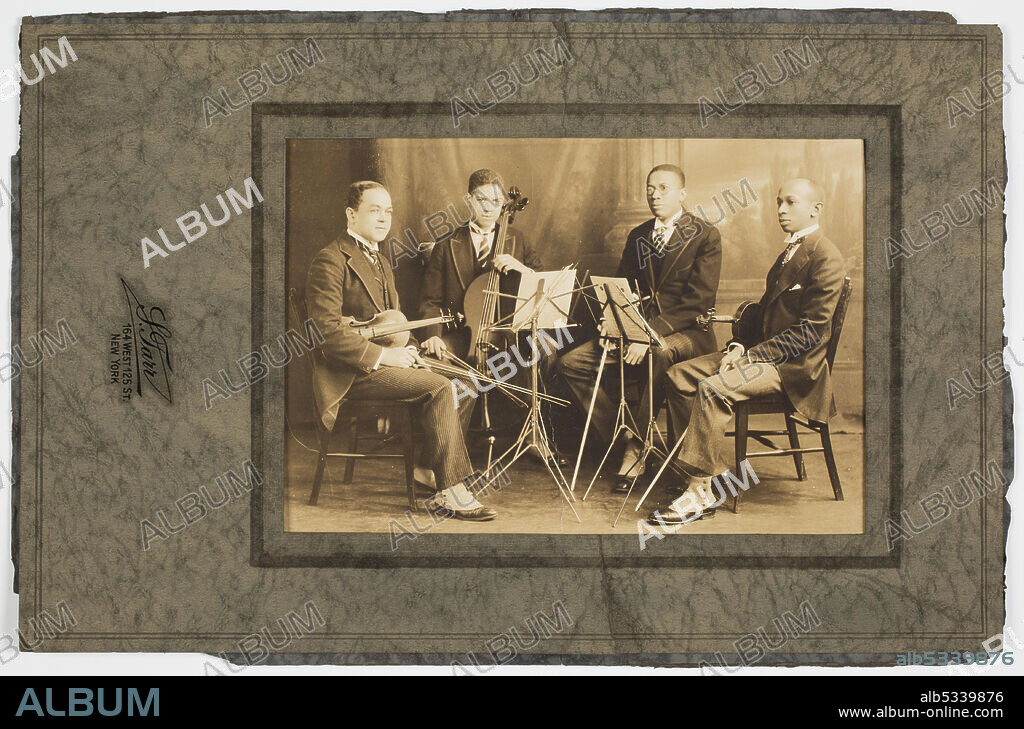 A photograph of the Negro String Quartet. The photograph features four men sitting in chairs positioned in a semi circle around two music stands. The men are all dressed in suits. The men from left to right are: Felix Weir, Marion Cumbo, Hall Johnson, and Arthur Boyd. The photograph isin a green/gray paper frame. A stamp on the front of the paper frame reads: [S. Tarr / 164 West 125 St. / NY]. The back of the frame is blank.