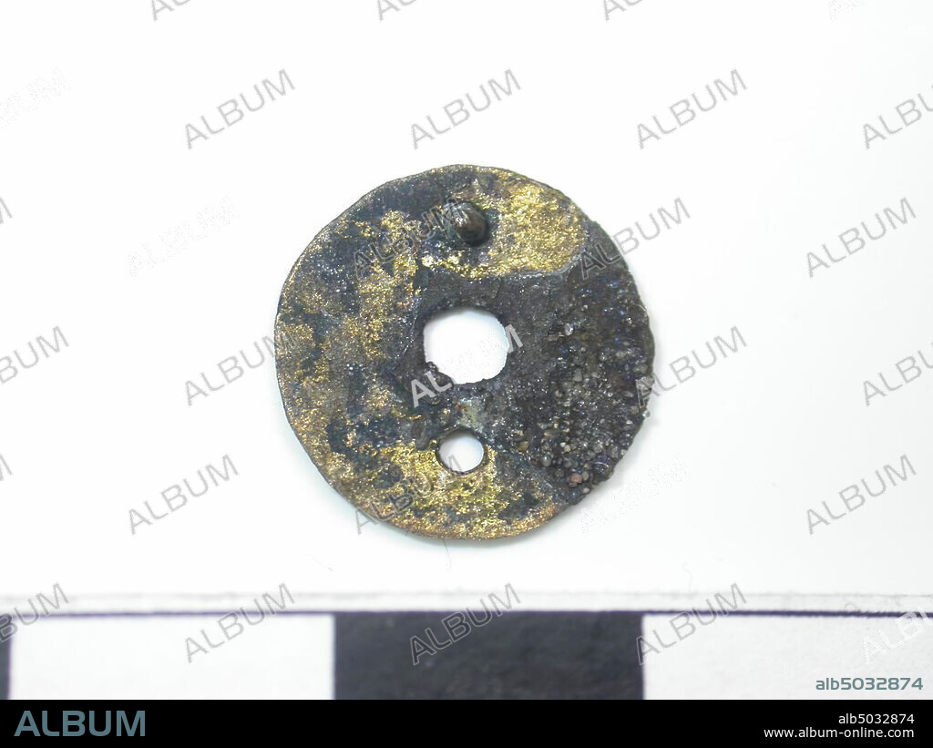 Circle with hole in the middle, gold-colored (copper alloy). Black touch on the surface. Back is flat. 2 pin mounting. A pin is missing, and there is a hole there. Pin is round. Pin length is 0.15. Diameter pin is 0,1 cm. Diameter hole is 0.3 cm., Belt stroke, metal, copper alloy, Dm: 1.3 cm, D: 0.05 cm, end of the 14th century 1350-1400, the Netherlands, Zeeland, Hulst, Verdronken Land.