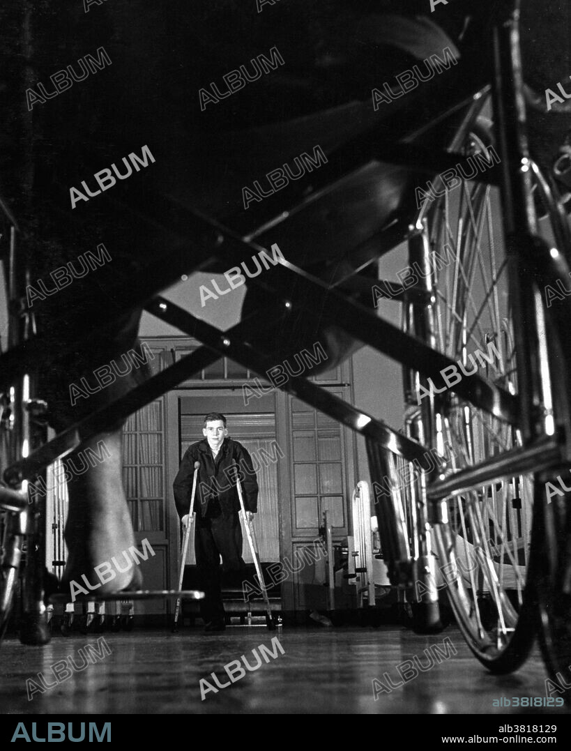 Caption: "Wounded soldiers use wheelchairs and crutches until they learn how to walk with a synthetic limb. Pfc. Charles Woody, injured near Taegu, walks on crutches. Walter Reed Military Hospital Washington, DC. December 8, 1950." Photograph credited to USIA.