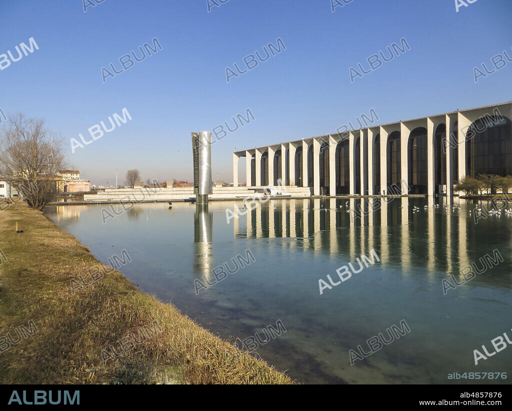 Segrate, Province of Milan, Lombardy, Italy.. Palazzo Mondadori, by Oscar Niemeyer, 1968 - 1975. The palace, home of the Italian publishing house Mondadori, during a winter day with the frozen lake. In the middle of the lake the sculpture by Arnaldo Pomodoro "Colonna a grandi fogli" (1972-1975) in bronze and steel, with dimensions of 13 2,20 2,20 meters.