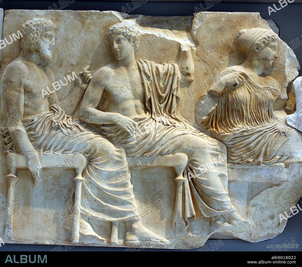 In the left section of the scene, Poseidon holding a trident and Apollo holding a laurel branch with the other. beside them sit two sister divinities, Artemis and Aphrodite. Parthenon Frieze Athens.