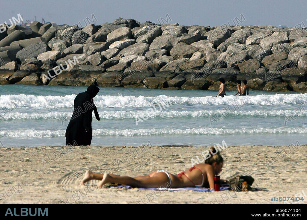 A traditionally clothed Arab women walks along the beach while a female tourist takes a sunbath wearing a bikini at the Jumeirah Beach in Dubai, UAE, 08 January 2007. Photo: Daniel Karmann. 08/01/2007