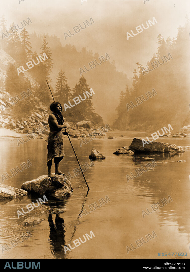 Edward S. Curtis Native American Indians - Hupa man with spear, standing on rock midstream circa 1923.