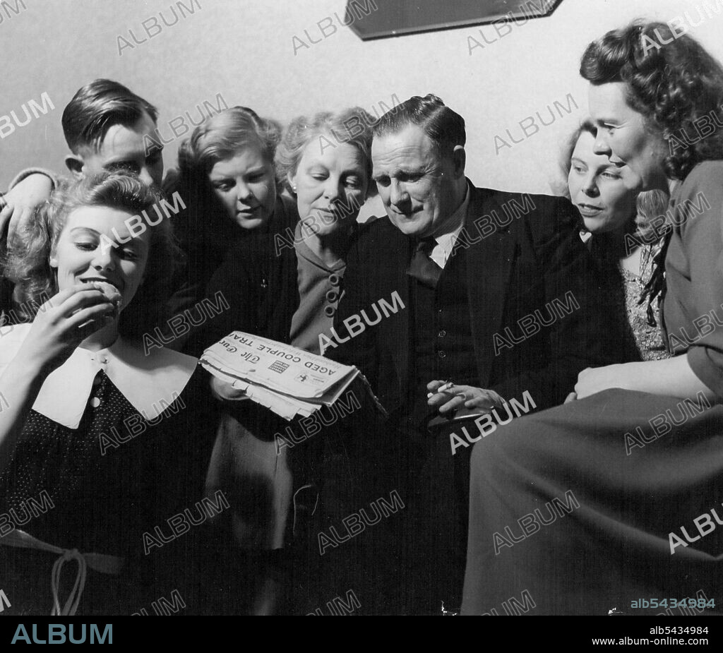 Margaret of the "Windmill" -- Margaret serenely muches a doughnut while proud family gather around daughter's latest press photograph. It seems she's made the front page again. F.l.t.r., Margaret, brother Cyril, aged 26, little sister Desni, 15, Mother Mabel, 55, Father George Edward, 57, married sister Barbara, 28, and Myrtle, 31. February 27, 1952. (Photo by Tom L. Balu, Camera Press).