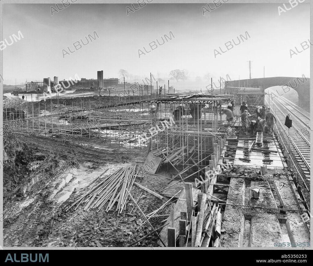JOHN LAING PLC. A view of the construction of the Stafford By-pass on the Birmingham to Preston Motorway (M6), showing Bridge 302 being built over the main Stafford-Wolverhampton railway, looking along the railway line in the direction of Wolverhampton and showing the Dunston Farm access bridge nearing completion. The work on the Stafford By-pass started in June 1960 and was opened to traffic in August 1962.