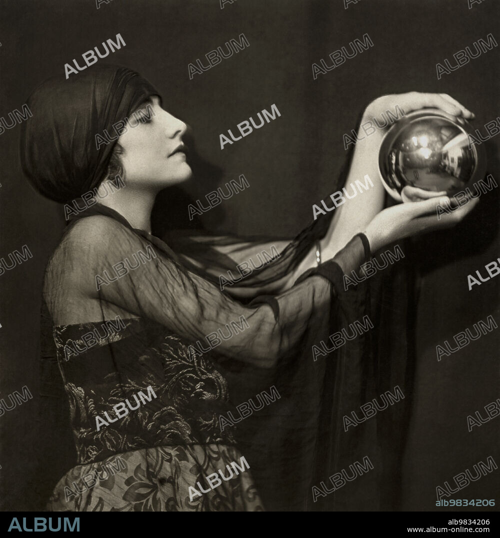 London, England c. 1920. Silent film actress Manora (aka Manvia)Thew gazes at the mystic in a crystal ball that she is holding in her hands. Photograph by Emil Otto Hoppe.
