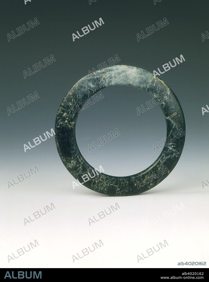 Dark green jade bracelet, Shang dynasty (Erligang Phase), China, c1600-c1400 BC. A bracelet of good even dark green colour with black flecks appearing to be almost black green overall. The smooth surface comes to a gently rounded outer edge.
