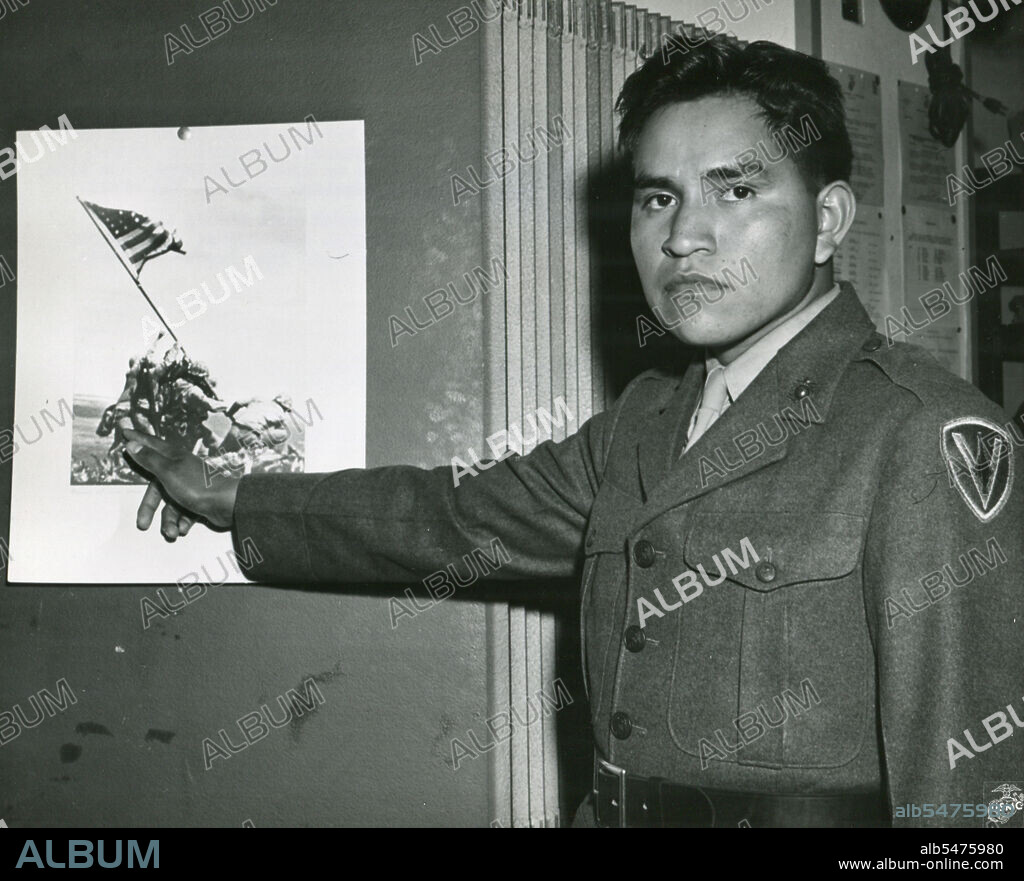 Marine Private First Class Ira Hayes illustrates the part he played in the raising of the Stars and Stripes on Mount Suribachi, Iwo Jima by pointing to his image on the historical photo of the event. 1945.
