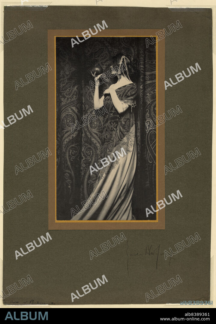 ZAIDA BEN-YUSUF. The odor of pomegranates, c1900. Photograph shows a woman wearing a long flowing gown, standing in front of curtain, facing left, holding a pomegranate.