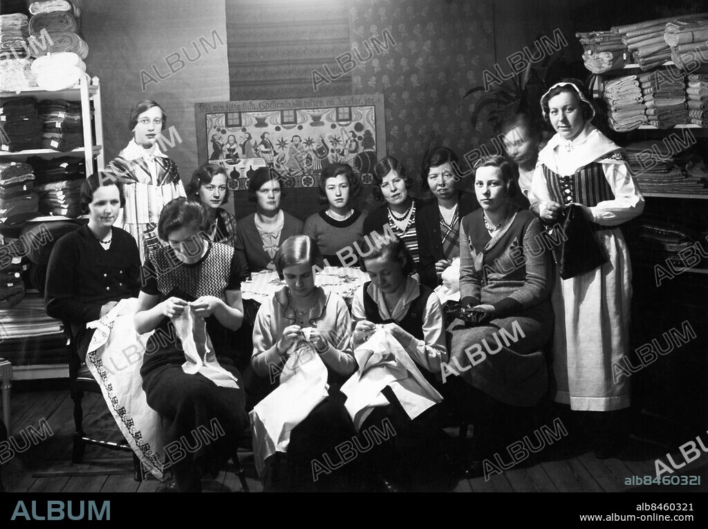 VÄSTERVIK 1933-06-22.. Orig. bildtext... VÄSTERVIKS 500-ÅRSJUBILEUM. I Västervik rustar man för fullt för att värdigt begå stadens 500-årsjubileum. På jubileumsdagen - den 22 juni - öppnas som bekant även en utställning. En detalj i jubileumsprogrammet, som väntas bli av en originell och mäktig verkan, är Tjustkvinnornas festliga tåg till jubileumsstaden, i vilket man väntar att minst 500 i Tjustdräkt klädda kvinnor skola deltaga. Ute i Tjustsocknarna pågår ett intensivt förarbete härför. Här sys det Tjustdräkter i långa banor! Damen t.v. bär sommar- och damen t.h. vinter-Tjustdräkten. Anm. Folkdräkter Sömnad Broderier CD89 sites: VÄSTERVIK ;SVERIGE.