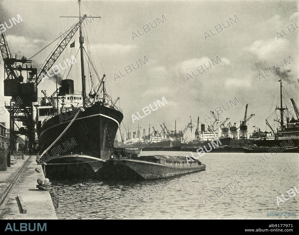 J DIXON-SCOTT. Merchants Bring In Wares By Ships from Every Nation Vessels alongside the Quays, King George V Dock', 1937. Cargo ships on the River Thames in London. From "The Said Noble River", by Alan Bell. [The Port of London Authority, London, 1937].