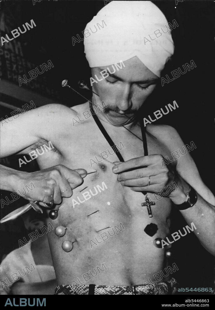 The Does This For A Living - Yvon Yva Phshes into his body the pong pins and Stiletto before taking his place in the glass case. Fakir Yvon Yva was placed in a glass fronted box at the Etoile Theatre, in Paris yesterday. He intends to stay ther for over a month without food. and to make it just that bit more difficult he has put lung pins through the skin on his neck and chest and a stiletto through his breast. November 06, 1954. (Photo by Paul Popper Ltd.).