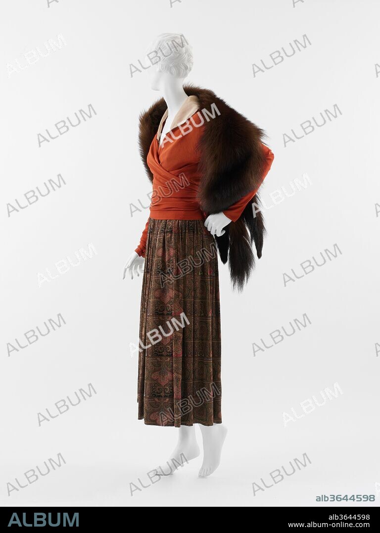 "Feuille d'automne". Culture: French. Designer: Paul Poiret (French, Paris 1879-1944 Paris). Date: 1916.
The day ensemble 'Feuille d'Automne' (Autumn Leaves), introduces the new, slightly raised hemline of the season. While Denise Poiret had worn boots à la Russe for years, they were especially apt when coordinated with ankle-exposing skirts. As with many of Poiret's designs, this ensemble acknowledges the prevailing mode while modifying it to the idiosyncratic sensibility of the designer. In the early 1920s, Poiret was to advocate panniered (wide-hipped) and crinolined silhouettes, but in this period - when many design houses endorsed a full, umbrella-shaped skirt - Poiret insisted on a line that cleaved reasonably to the body. There is fullness in the paisley-patterned skirt, but because it is not supported by petticoats, it collapses into the slender and natural line advocated by the designer and preferred by his wife. 
The surplice blouse wraps at the waist, anticipating the body-conforming styles of the 1930s by more than a decade. Vogue noted in the early 1920s that among Poiret's greatest innovations was the "kimono neckline." By adding a white collar to the surplice, Poiret co-opts the Asian origins of the garment's construction and situates it in the tradition of Western fashion. In this ensemble, as in others, Denise Poiret's sylphlike form encouraged innovation. The wrap front of the blouse would not have been adequate for the fuller form of the Belle Époque ideal, but for the slender build of Poiret's wife, the adjustability of the wrap provided the minimum of support for the suggestion of a natural bustline.