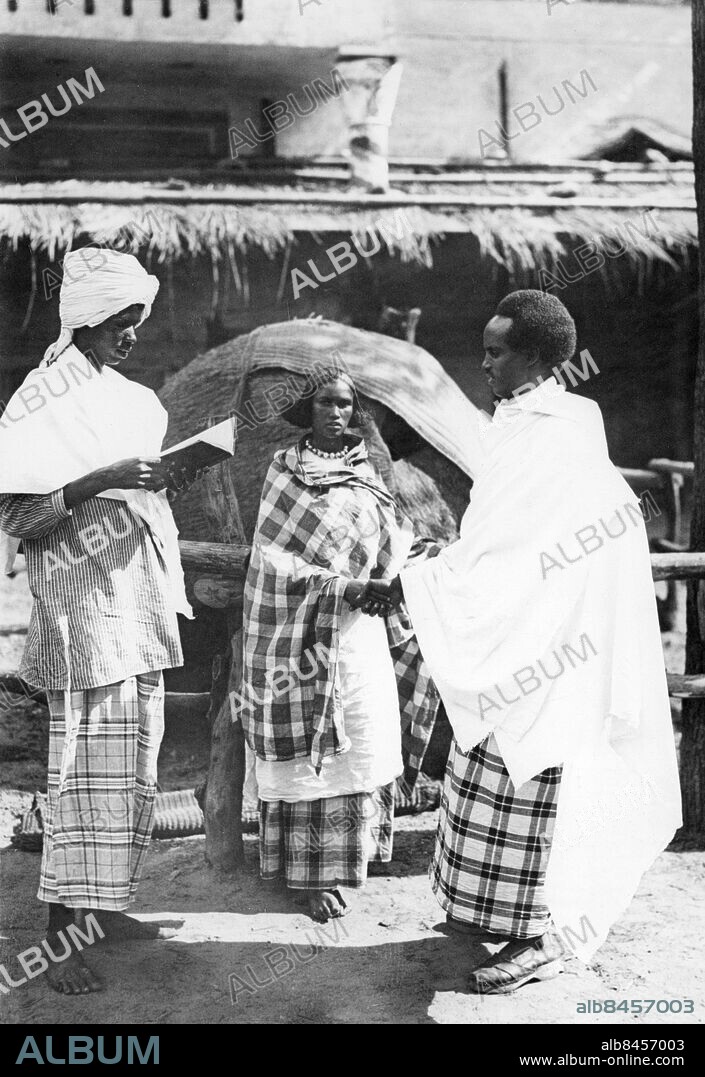 Orig. bildtext... QUAINT CEREMONIES AT SOMALI WEDDING N BERLIN ZOO. The Berlin Zoo today witnessed the strangest ceremonies it has ever seen when two members of the Somali group now living at the Zoo, Ali Hersi, the Chief of the group, and Amina Hassan, the prettiest chocolate colored maiden of the tribe, became Somali man and wife after going through the whole picturesque native ritual, dances, songs and a feast of goat roasted over an open fire. Photo shows: Ali Hersi and Amina Hassan being wedded by a native preacher who reads from the bible while demure bride and proud bridegroom listen attentively. Anm. CD66 sites: AFRIKA* ;BERLIN ;SOMALIA* ;TYSKLAND.