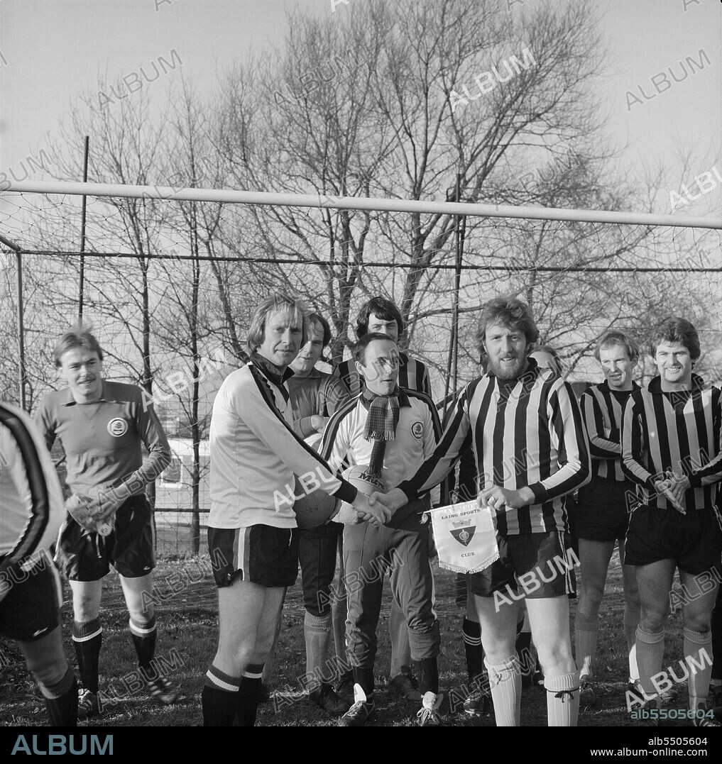 JOHN LAING PLC. Laing Sports Ground, Rowley Lane, Elstree, Barnet, London, 07/12/1980. Chris Martin, Laing's team captain, shaking hands with Dennis Waterman while holding a Laing Sports Club pennant before a charity football match at the Elstree Sports Club. An estimated 300 people attended the December 1980 charity football match between a team of Laing players and English actor Dennis Waterman's All Stars. The match was held to raise money for the Jerry Doherty Heart Fund. The game finished 2-2 and £452 in total was raised. Stars on Dennis Waterman's team included Jan Webster, ex-England rugby scrum half; Danny Rioch, ex-Aston Villa; Jonathan Kyd, from children's TV programme Pipkins; John Inchmore, Worcester County cricketer; and Bob McNab, ex-Arsenal full back. Playing on the Laing side were Dave Hall, Tim Smith, Kevin Blande, Geoff Seager, Richard Sawyer, Chris Martin, Dave Offord, Graham Hollis, Will Kellett, Mike Reed, Bob Louden, Dave Butcher and Phil Brown. This image was published in January-February 1981 in Laing's monthly newsletter 'Team Spirit'.