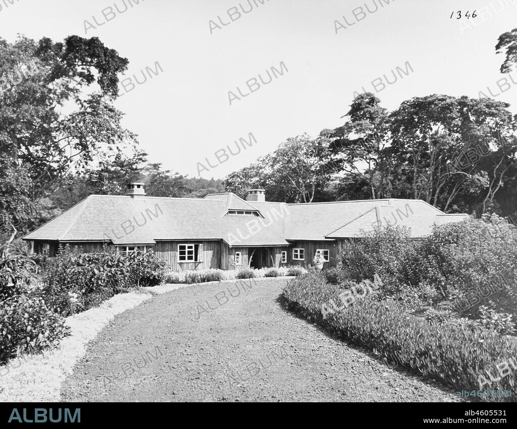 Kenya, View across gardens of Sagana Lodge, the "Royal Lodge" presented to Princess Elizabeth. The photograph shows a ground floor timber building with a tiled roof set amongst trees and copious flower boundaries. A gravel circular drive curves in front of the building, February 1952. 2001/090/1/4/1/68.