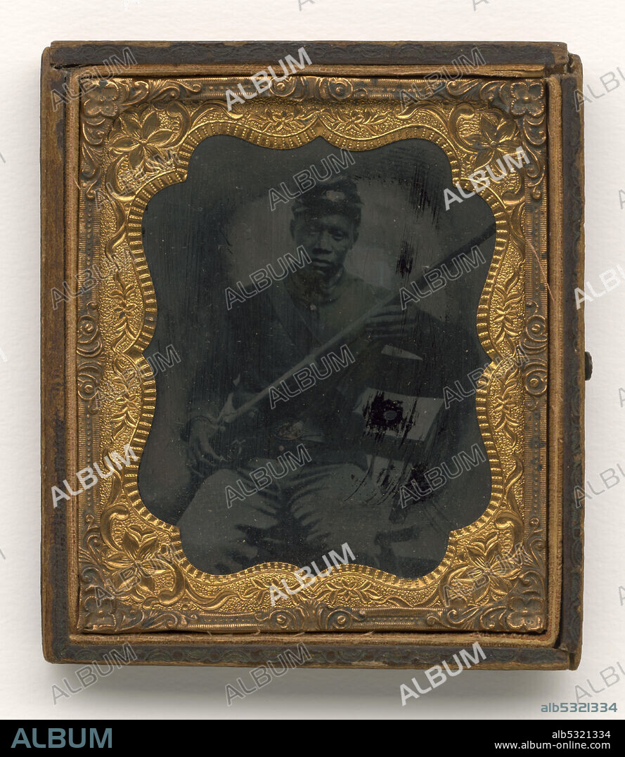 Ambrotype of an African-American soldier depicted seated on a wooden chair with one end of a P1853 Enfield musket held by his right hand near his right hip. The musket extends diagonally across his torso, its barrel held near his shoulder in the long fingers of his left hand; his left elbow rests on the top of the chair. He wears a dark-colored cap, dark-colored frock coat over a lapelled shirt, and light-colored trousers. His belt is closed with a metal plate buckle and a cartridge box belt crosses his chest. Metal on the uniform appears to have been touched up with gold paint, which has the unfortunate result of masking emblems on the kepi, belts, and buttons. The ambrotype is in a decorative gold case.