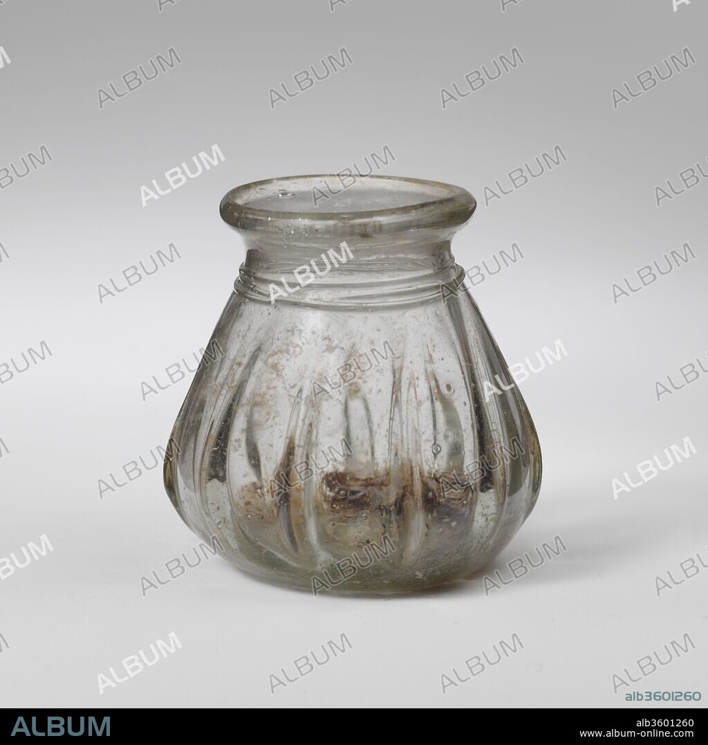 Glass jar. Culture: Roman, Eastern Mediterranean. Dimensions: 2 5/16 in. (5.8 cm)
Other: 2 3/16 in. (5.6 cm)
Diam. of rim: 1 1/2 in. (3.8 cm). Date: 3rd-4th century A.D..
Colorless with light green tinge, with same color trail and ribs.
Solid rim folded out, over, and in; short, concave neck; sides of body sloping out downward; pushed-in bottom with prominent pontil scar.
Slender trial wound three times around neck; eleven vertical, slightly slanting ribs of varying length on body.
Intact; some bubbles; little pitting and weathering.