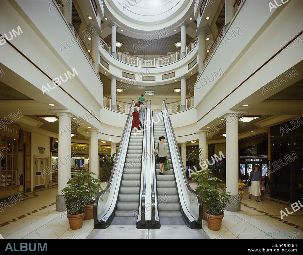 JOHN LAING PLC. Eldon Garden shopping centre, Percy Street, Newcastle upon Tyne, 03/07/1989. Shoppers using the escalators in the Rotunda section of the Eldon Garden shopping centre. The Eldon Garden shopping centre was a development of 42 shops over 3 storeys and a 477 space carpark.  Laing secured the £11.5m management contract for the construction in 1987 for Greycoat Shopping Plc.  Work began in January 1988 and the centre was open to the public from March 1989 and officially open by Princess Margaret in November 1989.  The development had to incorporate the existing pub, now called the Three Bulls Heads.  The pub was underpinned and supported whilst its roof was removed and rebuilt so that it was structurally independent of the shopping centre.  The Rotunda is roofed by a glazed dome and connected the two main shopping levels with the gourmet food hall on the ground floor.Eldon Garden is linked to the Eldon Square shopping centre by a 2 storey glazed mall that bridges Percy Street, this had to be constructed overnight when the road could be closed.
