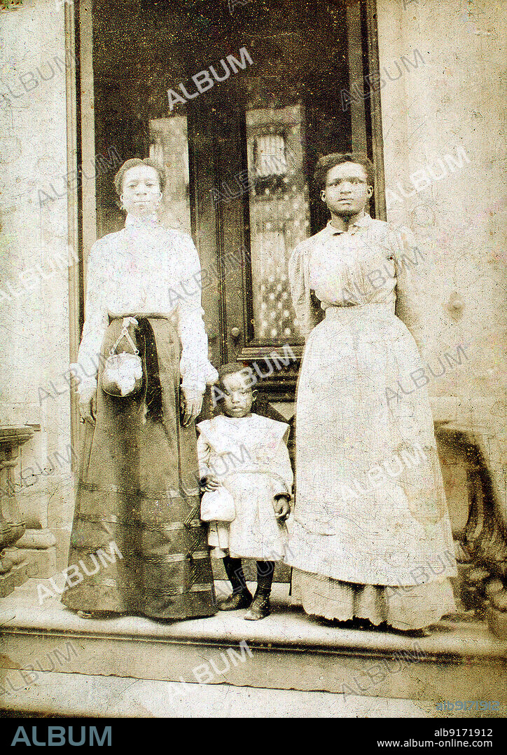 ECKEHARD MUNCK. Two women and a child standing on step in front of a doorway of a house, c1900.