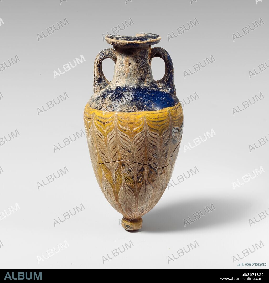 Glass amphoriskos (perfume bottle). Culture: Greek, Eastern Mediterranean or Italian. Dimensions: H.: 4 3/8 in. (11.1 cm). Date: 4th-3rd century B.C..
Translucent cobalt blue, with handles and base-knob in same color; trails in opaque yellow and opaque white.
Broad horizontal rim-disk with rounded edge; cylindrical neck, expanding slightly downwards; broad, sloping shoulder; elongated ovoid body, tapering sharply downwards; applied small circular base-knob with uneven bottom; two strap handles applied to shoulder and drawn up, turned in, and pressed on to neck.
One fine white trail attached at edge of rim-disk; a yellow trail applied to top of body and wound spirally, at first in a horizontal line, then tooled into a feather pattern, with alternating upward and downward strokes, the former making slightly raised knobs, the latter shallow indents around top of body; a second trail in white added around upper body, forming alternating bands with the yellow trail; both trails continuing to bottom; on base-knob, three stratified eyes, comprising an outer circle and central dot in translucent blue and broader inner circle in opaque white.
Broken and repaired around body, and one quarter of rim-disk missing; some dulling and patches of creamy iridescent weathering.