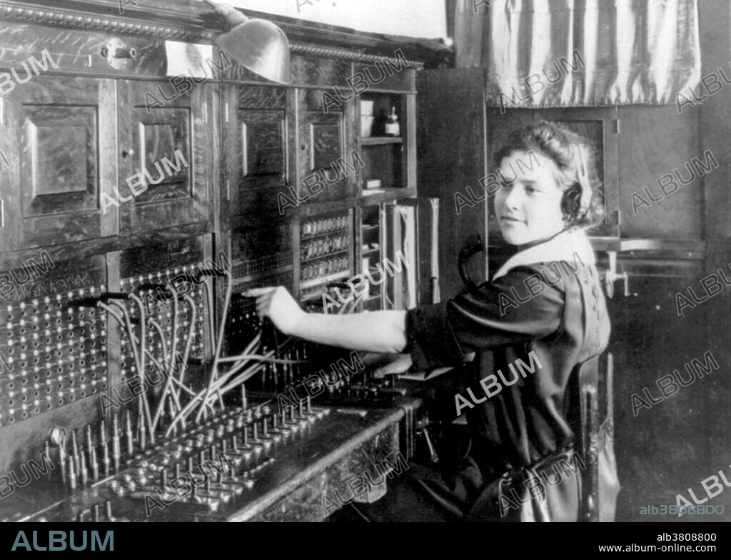 In the early days of telephony companies used manual telephone switchboards, and switchboard operators connected calls by inserting a pair of phone plugs into the appropriate jacks. Each pair of plugs was part of a cord circuit with a switch associated that let the operator participate in the call. Each jack had a light above it that lit when the telephone receiver was lifted. Lines from the central office were usually arranged along the bottom row. Before the advent of automatic exchanges, an operator's assistance was required for anything other than calling telephones across a shared party line. Callers spoke to an operator at a Central Office who then connected a cord to the proper circuit in order to complete the call. Automatic, or Dial systems were developed in the 1920s to reduce labor costs as usage increased, and to ensure privacy to the customer. Companies observed that women were generally more courteous to callers. However, a contributing factor to women entering this workforce was because women were paid from one half to one quarter of a man's salary. Photographed by J. F. Anderson, St. Marie's, Idaho, 1922.