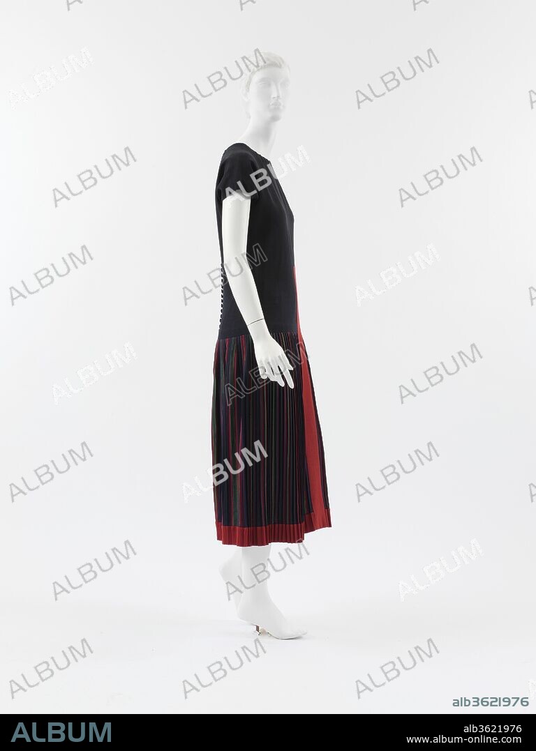 Mademoiselle. Culture: French. Designer: Paul Poiret (French, Paris 1879-1944 Paris). Date: 1923.
Two distinctive styles emerged in the early 1920s. One, with a panniered skirt and exaggerated hips, was called the "robe de style." The other, which was the style that prevailed, was the straight-lined shift called the "chemise." In another instance of the couturier's insistence on the independent creative vision of the artist, Poiret, for much of the last decade of his career, proffered styles that had a rounded silhouette with full dirndl skirts à la Bretonne. Despite his deliberate intransigence in the face of the overwhelming trend to the planar silhouette, even Poiret, at least in some of his collections, conceded to the fashionable taste of the day. 
'Mademoiselle' is a compromise between his advocacy of fullness in the skirt and the willowy silhouette in vogue. From the wardrobe of Denise Poiret, the dress would have been enhanced by her lithe form and feline grace, attributes commented on by her contemporaries. Poiret dismissed the more androgynous fashion à la garçonne promoted by Jean Patou and Coco Chanel, which minimized the contours of the chest and hips. "Cardboard women," he called them, with "with hollow silhouettes, angular shoulders and flat breasts ... birds:" In his rendering of the suppressed fit, the shoulder line is sloped, the natural waist is articulated by a slight curvature in the side seam, and the skirt consists of a tightly pleated striped wool, introducing a fullness that retracts on itself. The linearity of the dress is augmented by an insertion of a red wool stripe that extends down the center front of the dress, beginning at just above the natural waistline and extending down into the hem of the skirt. Arbitrary and purely decorative, the stripe suggests the formal interplay of geometries in a Constructivist painting.