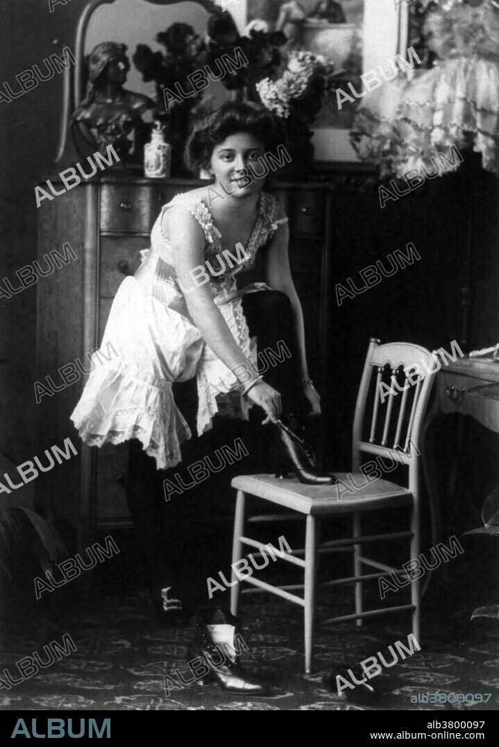 Entitled: "Young woman in glamorous, erotic poses: 'Late for Breakfast' - in negligee, putting on high-button shoes." Fashion is a popular style or practice, especially in clothing, footwear, accessories, makeup, or furniture. Fashion is a distinctive and often habitual trend in the style in which a person dresses. It is the prevailing styles in behavior and the newest creations of textile designers. Prior to the mid-19th century, most clothing was custom-made. It was handmade for individuals, either as home production or on order from dressmakers and tailors. By the beginning of the 20th century, with the rise of new technologies such as the sewing machine, the development of the factory system of production, and the emergence of department stores, clothing had increasingly come to be mass-produced in standard sizes and sold at fixed prices. Photographed by William H. Rau, 1901.