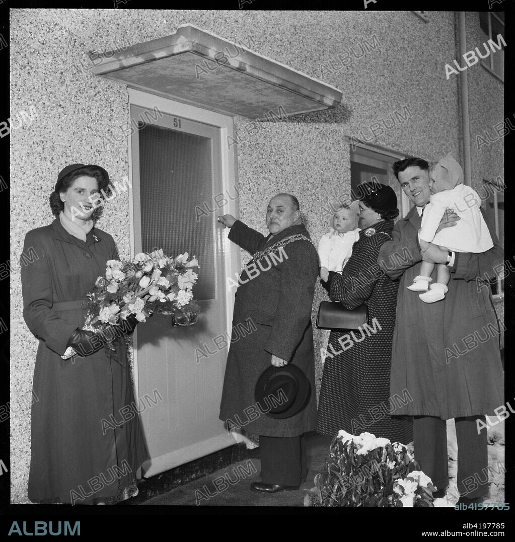 House opening ceremony, Ramsbury Avenue, Penhill, Swindon, Wiltshire, 1955 Mayor of Swindon Arthur Madge Bennett ceremonially opening the front door of the 3000th post-war house to be constructed in the town, whilst a family waits behind. The original Laing handlist records the subject for this image as 'Opening of 3000th house at Swindon'.
