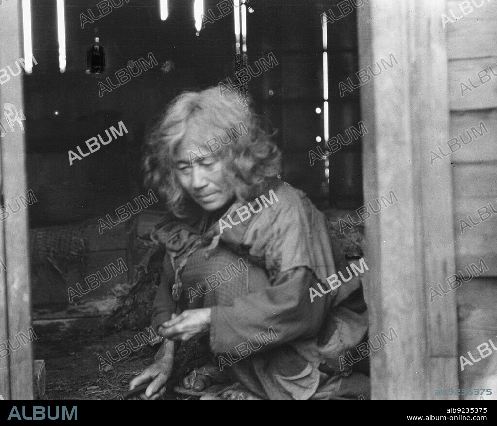 ARNOLD GENTHE. Ainu woman seated in the doorway of a wooden hut, 1908.