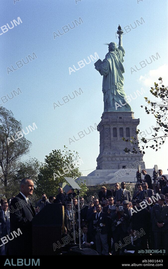 President Johnson speaking to assembled crowd before signing the Immigration Act. Liberty Island, NYC, October 3, 1965. Immigration and Nationality Act of 1965, also known as the Hart-Celler Act, abolished the national origins quota system that was American immigration policy since the 1920s, replacing it with a preference system that focused on immigrants' skills and family relationships with citizens or U.S. residents. The 1965 act marked a radical break from the immigration policies of the past. The law as it stood then excluded Asians and Africans and preferred northern and western Europeans over southern and eastern ones. At the height of the civil rights movement of the 1960s the law was seen as an embarrassment by, among others, President Kennedy, who called the then-quota-system "nearly intolerable". After Kennedy's assassination, President Johnson signed the legislation into law, saying "This system violates the basic principle of American democracy, the principle that values and rewards each man on the basis of his merit as a man. It has been un-American in the highest sense, because it has been untrue to the faith that brought thousands to these shores even before we were a country". Photographed by Yoichi Okamoto October 3, 1965.