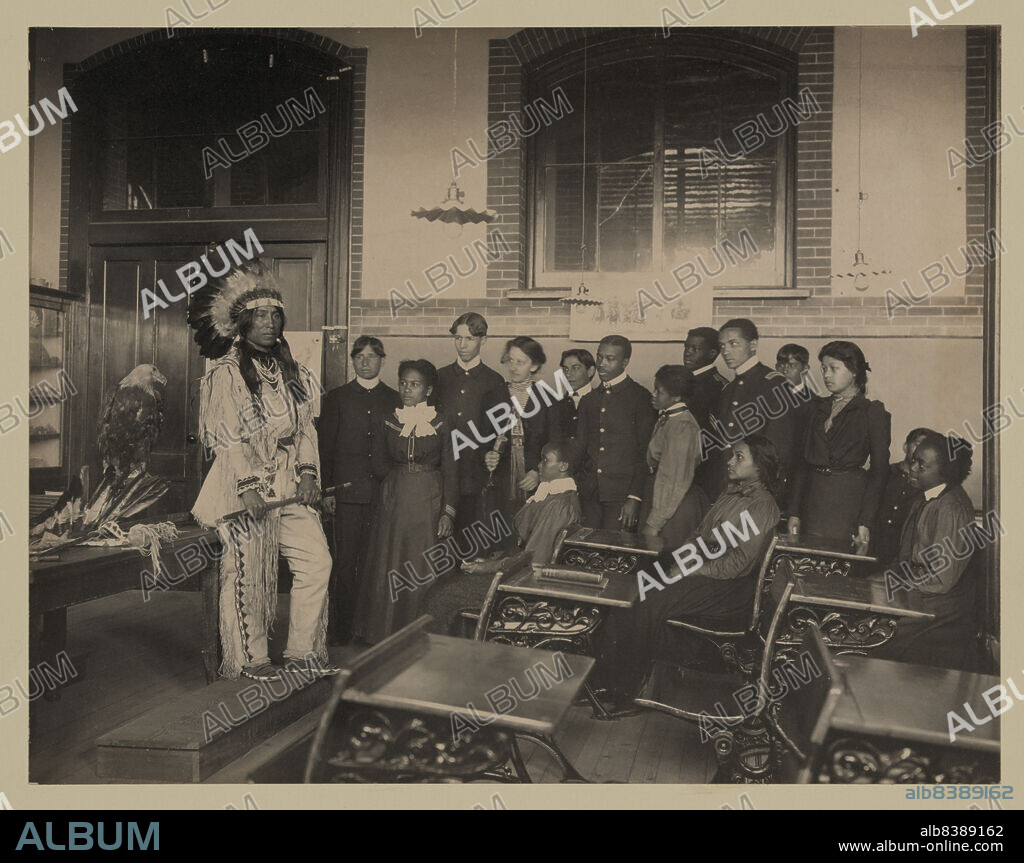 FRANCES BENJAMIN JOHNSTON. Louis Firetail (Sioux, Crow Creek), wearing tribal clothing, in American history class, Hampton Institute, Hampton, Virginia, 1899 or 1900.